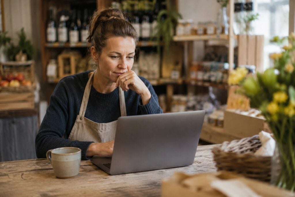 A shop owner weighing up options on a laptop at the counter